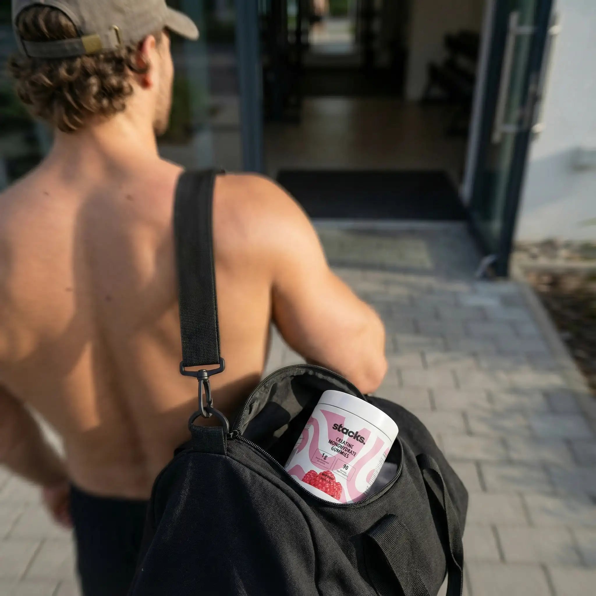 Sportler geht ins Gym, eine Dose stacks Creatin Gummies ragt aus seiner Sporttasche