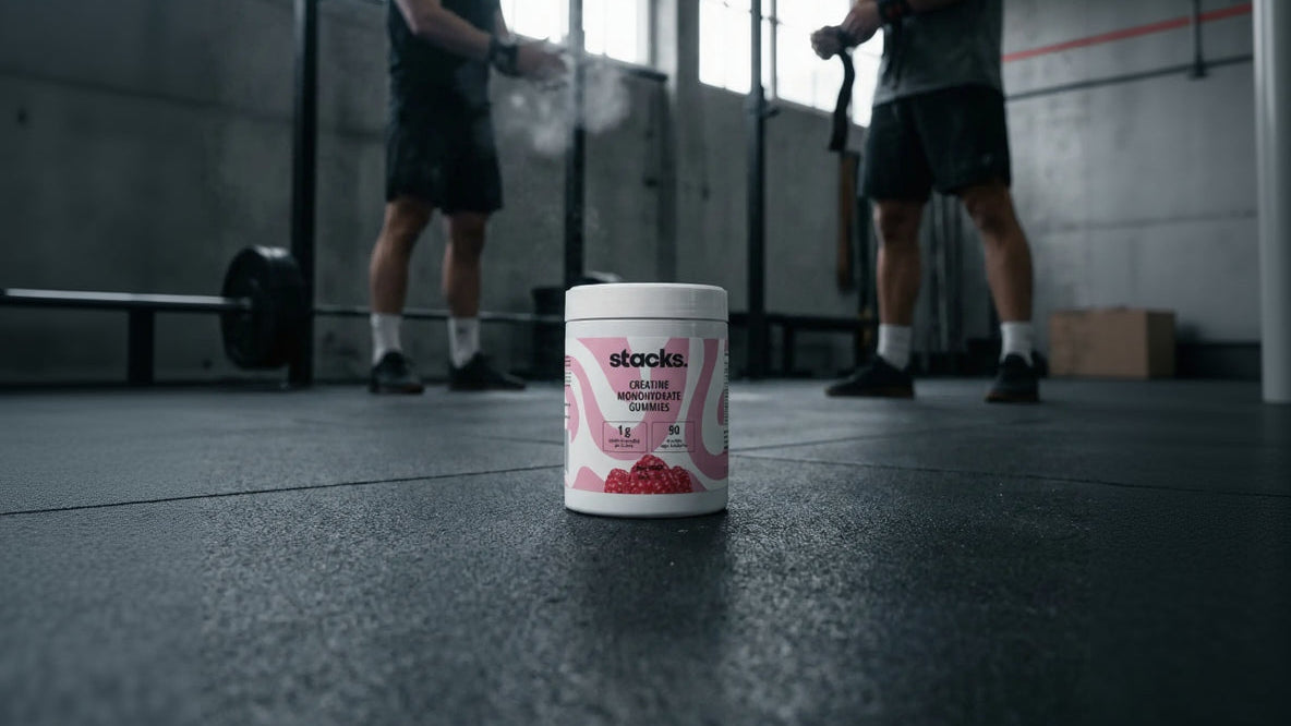 Dose stacks Creatin Gummies im Gym, zwei Athleten klatschen sich im Hintergrund ab.