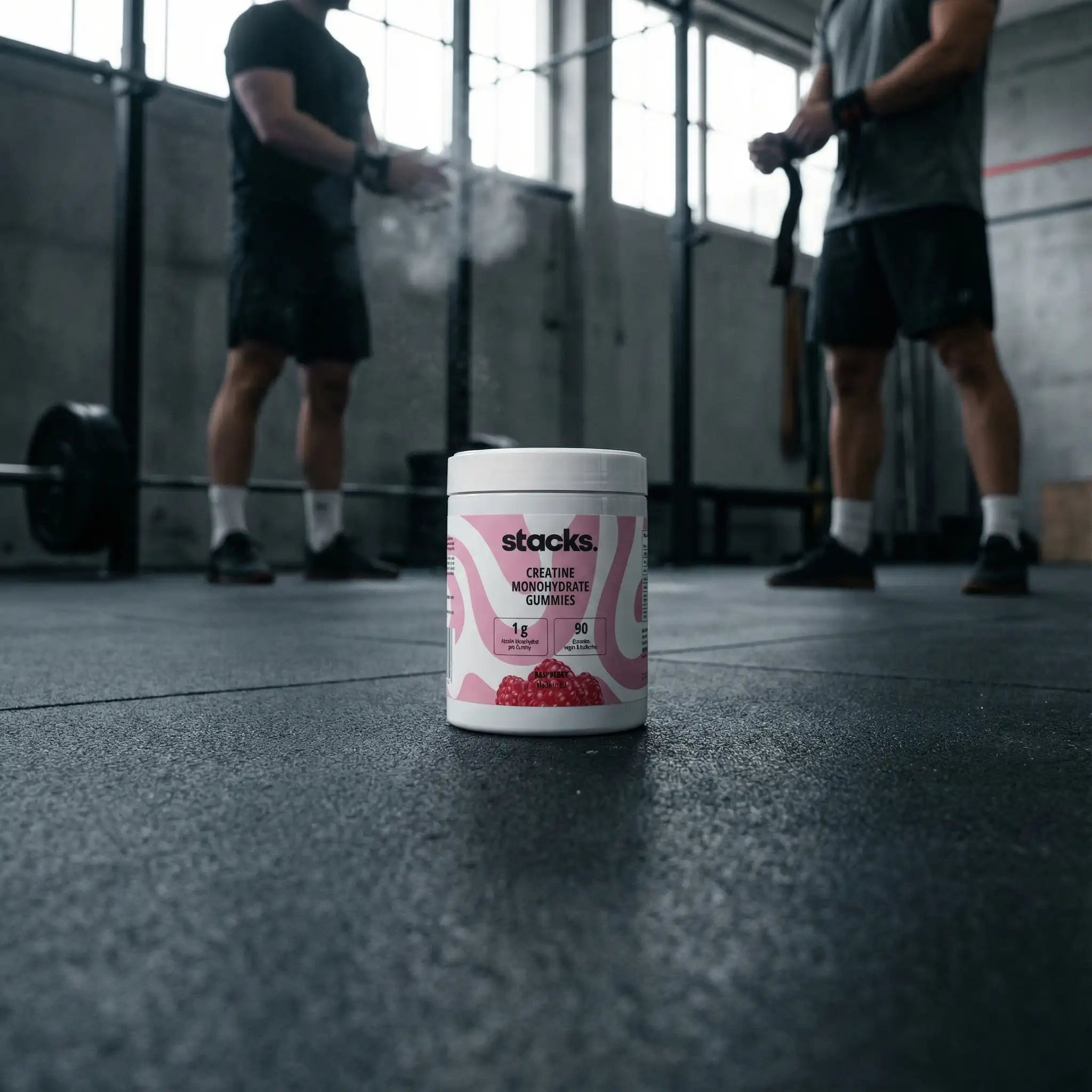 Dose stacks Creatin Gummies im Gym, zwei Athleten klatschen sich im Hintergrund ab.