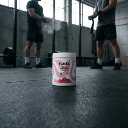 Dose stacks Creatin Gummies im Gym, zwei Athleten klatschen sich im Hintergrund ab.